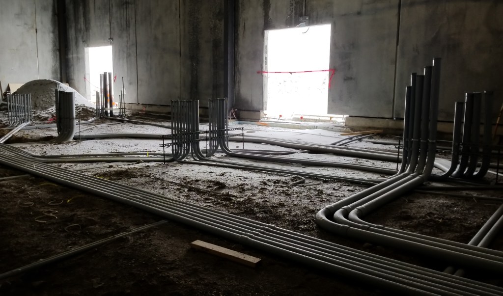 A dimly lit room with exposed pipes and a large, illuminated doorway.