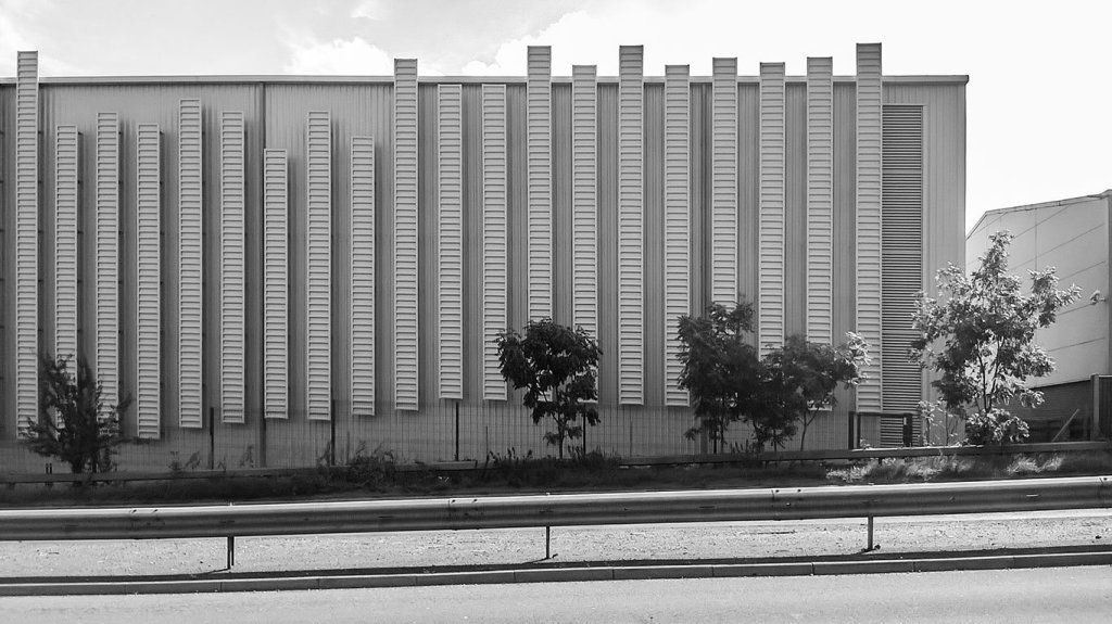 An industrial building from afar, partially obscured by ground-level trees. Grouped to the right, copious vertical rows of...