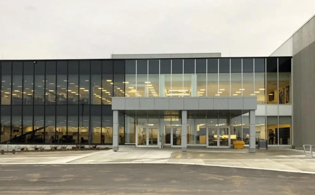 A modern commercial or office building, featuring a sleek black facade and a spacious glass entrance with an overhang and ...