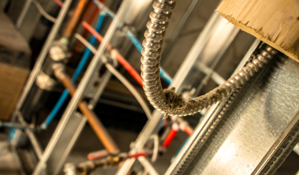 A room with exposed pipes, likely a mechanical basement area, featuring insulated and non-insulated pipes.