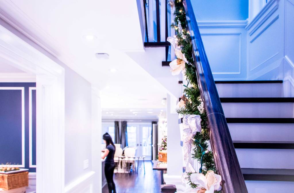 The staircase of a luxury home adorned with a Christmas garland, viewed from the first floor looking up toward the second ...